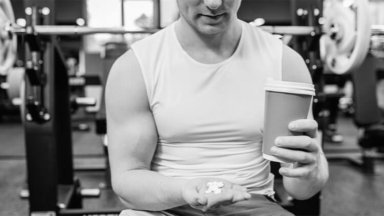 Aproximação dos braços desportivos do homem musculoso mostrando suplementos desportivos e de fitness